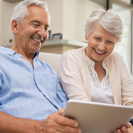 Ein älteres Paar schaut sich Inhalte auf einem Tablet an und ist dabei amüsiert.